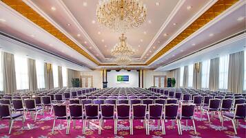 A conference room with rows of purple chairs, a large chandelier, and a screen at the front.