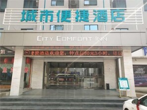 Entrada de un hotel con señalización para 'City Comfort Inn' y una pantalla digital con texto.