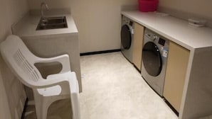 A compact laundry area with a washing machine, a sink, and a plastic chair. - City Comfort Inn Hotel (Wuhan)