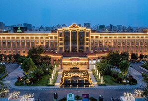 A large hotel with a central courtyard, multiple floors, and a city skyline in the background. - Crowne Plaza Zhengzhou by IHG (Zhengzhou)
