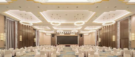 Un salón de conferencias amplio con un escenario, mesas redondas y sillas dispuestas para una reunión.