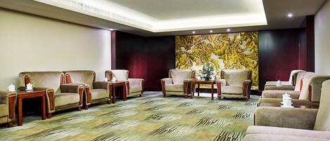 A hotel lobby with a patterned carpet, multiple seating areas, and a large decorative wall.
