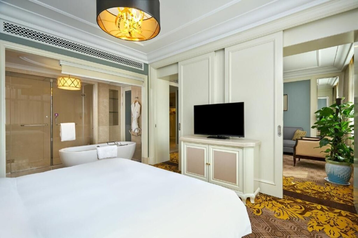 A hotel room with a large bed, a television, a bathroom with a bathtub, and a potted plant.
