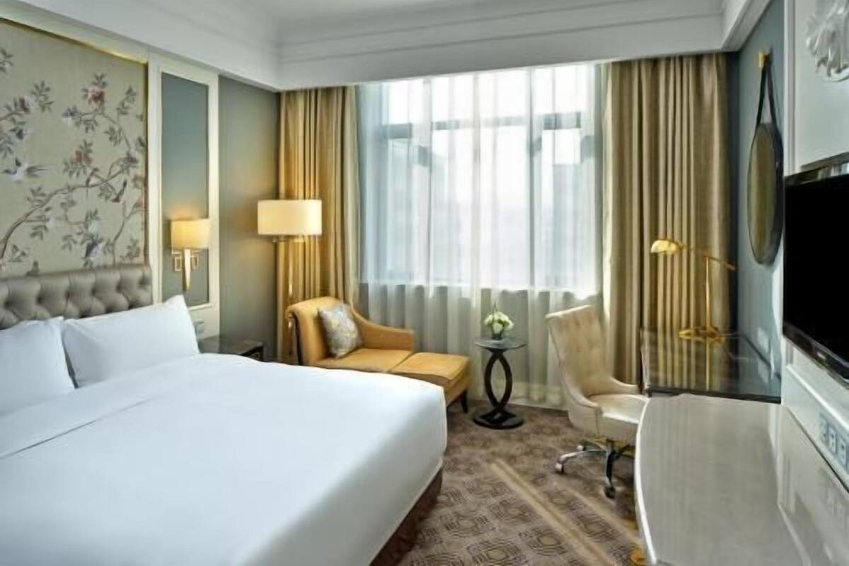 A hotel room with a large bed, a sofa, a chair, a TV, and a window with curtains.