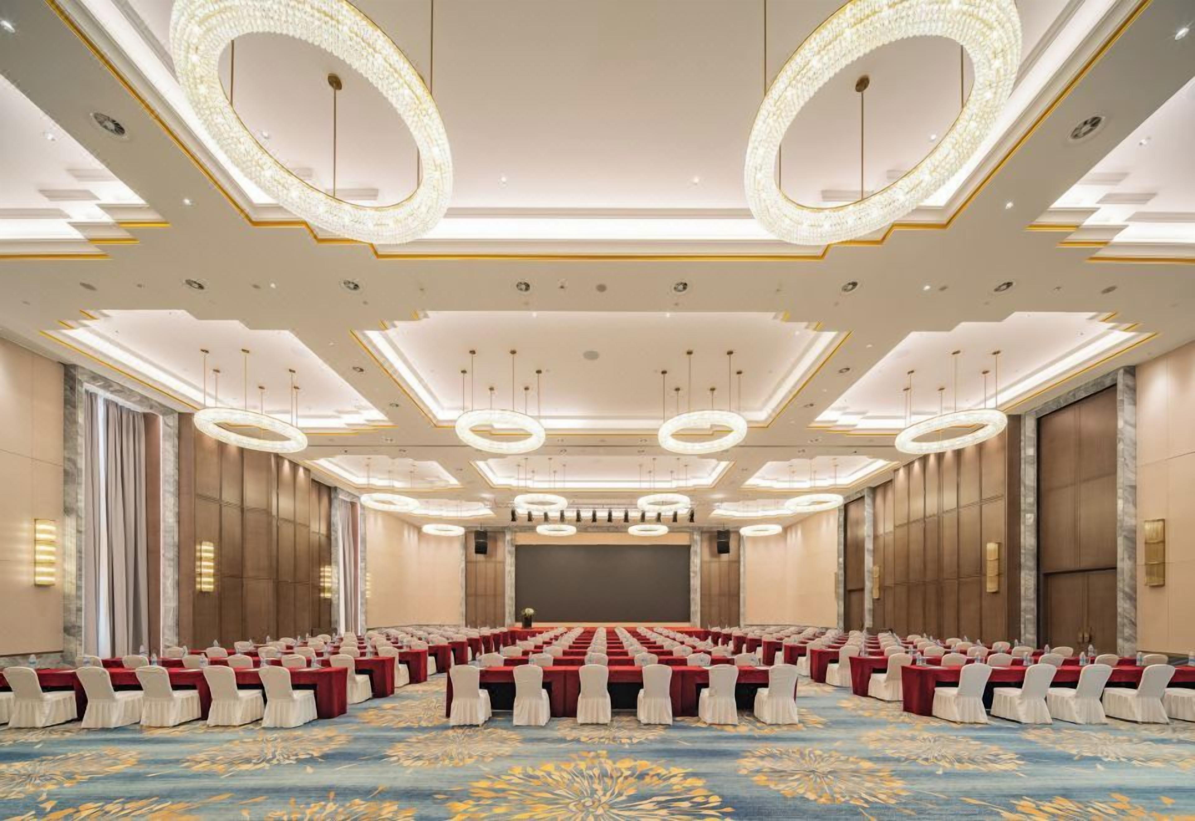 Una sala conferenze con file di tavoli, sedie e un grande schermo di fronte.