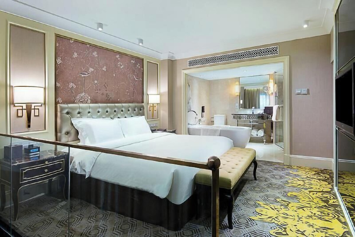 A hotel room with a large bed, bedside tables, a mirror, and a bathroom visible through an open door.