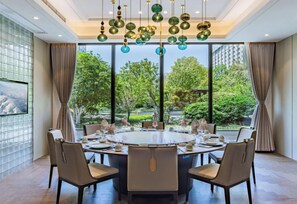 Uma sala de jantar com mesa redonda, cadeiras e vista para o verde lá fora.