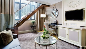 A living room with a staircase, a sofa, a glass coffee table with flowers, a desk with a chair, a TV, and a cabinet. - Crowne Plaza Zhengzhou by IHG (Zhengzhou)