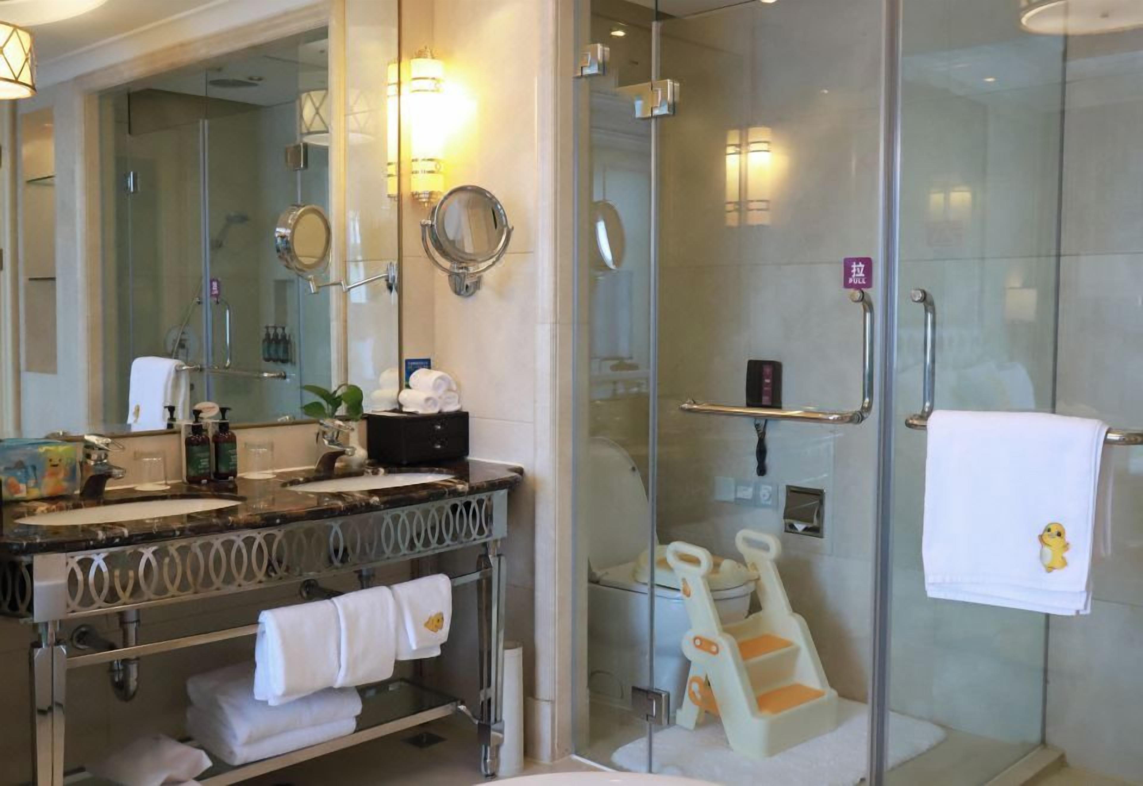 A modern bathroom with a glass-enclosed shower, a vanity with a mirror, and a toilet with a child seat.