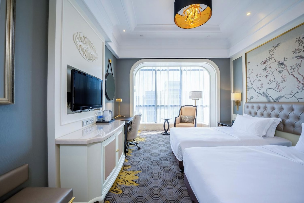 A hotel room with a bed, a desk with a TV, a chair, and a large window.
