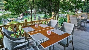 An outdoor dining area with a wooden table and wicker chairs, surrounded by greenery. - Crowne Plaza Zhengzhou by IHG (Zhengzhou)