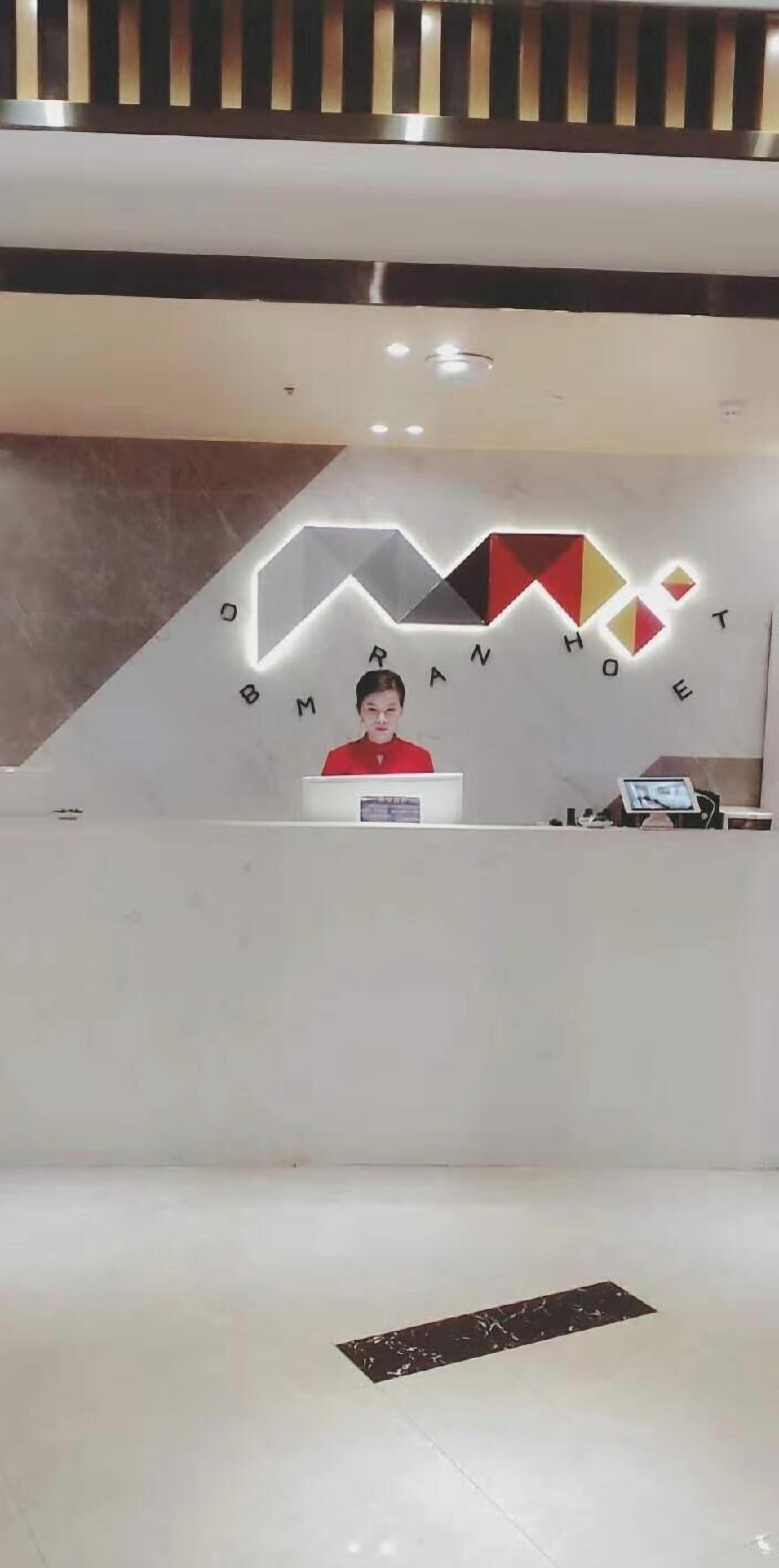 A reception desk with a logo above it, a person sitting behind the desk, and a floor plan in the foreground.