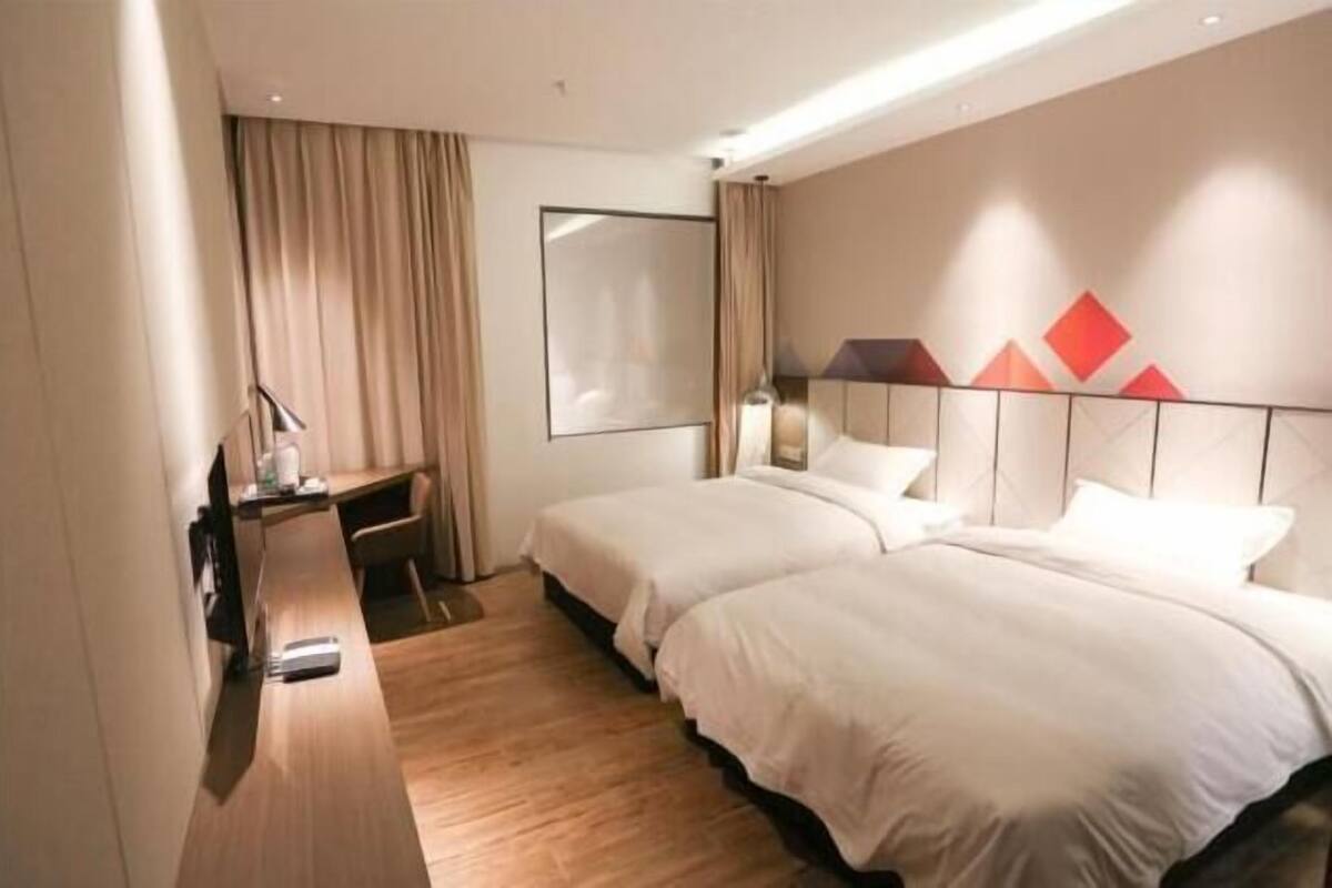 A hotel room with two beds, a desk, a chair, a lamp, and a window with curtains.