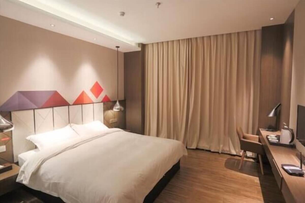 A hotel room with a bed, a desk, a chair, a TV, and curtains.
