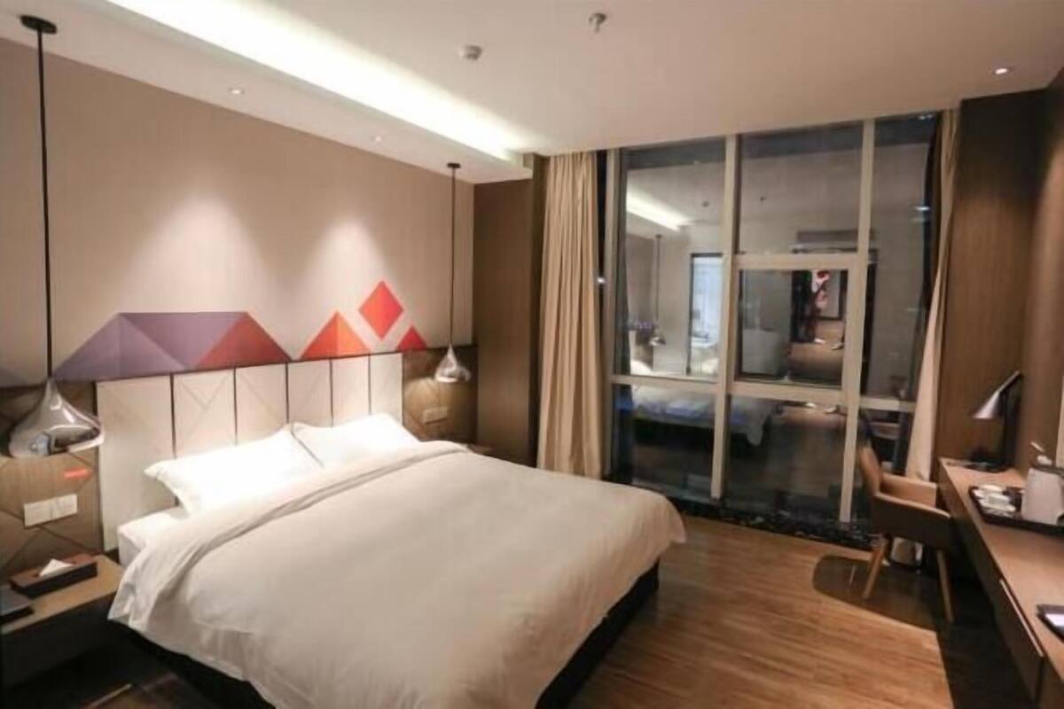 A hotel room with a bed, desk, and large window.