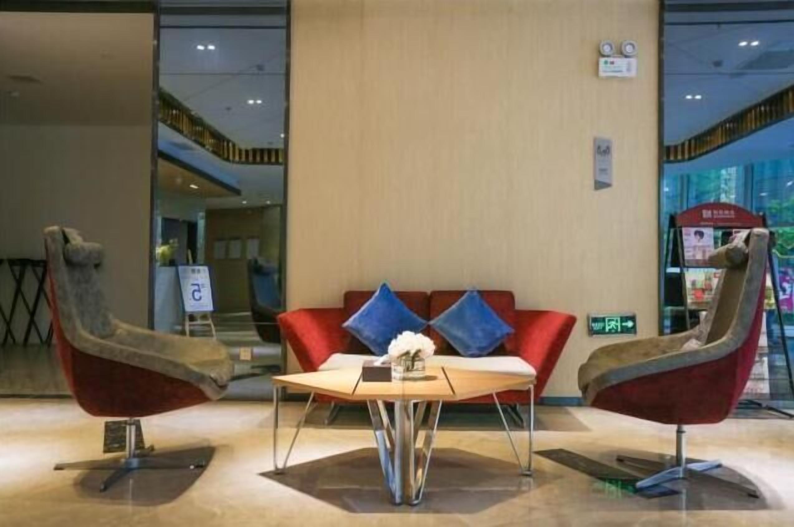 A lobby with a red sofa, two armchairs, a coffee table, and a small table with a vase.