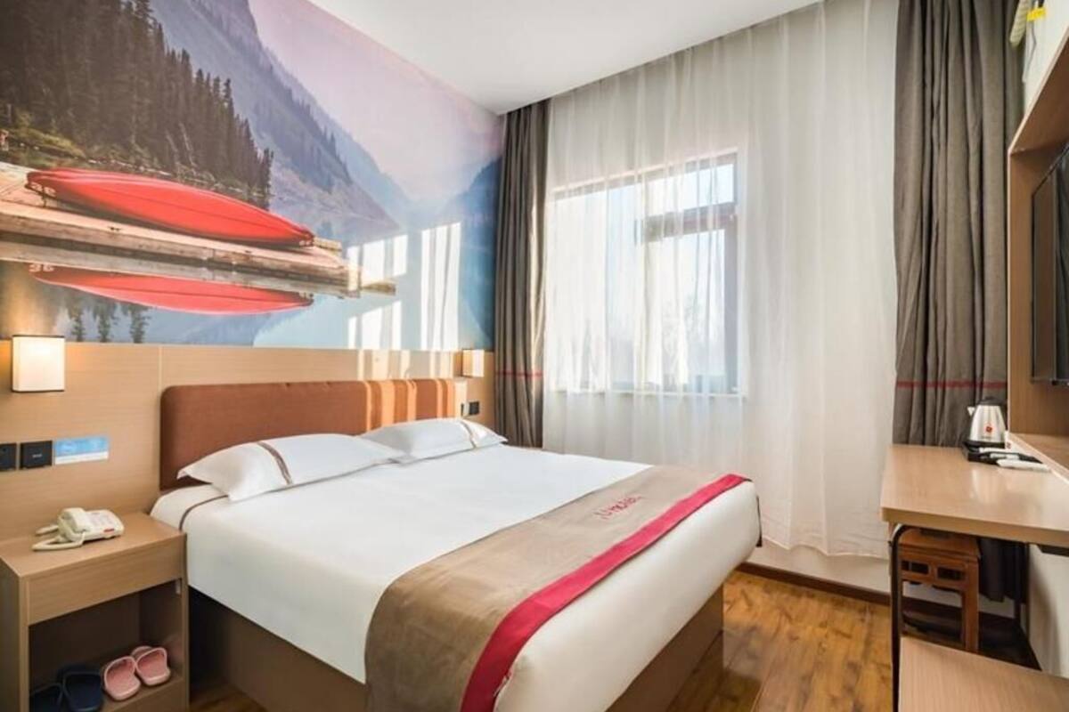 Una habitación de hotel con una cama, un escritorio, una silla, una mesita de noche y una pared con un mural decorativo.