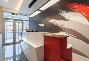 Ein Empfangsbereich mit modernem Design, inklusive einer Rezeption, einem Glastür-Eingang und einer Wand mit abstrakter Kunst.