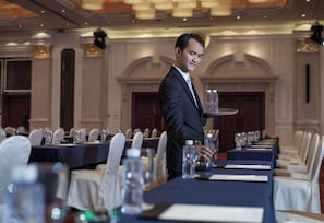 A formal dining room with long tables set for a meal, a waiter serving, and a classic interior design. - Holiday Inn Foshan Nanhai Central by IHG (Foshan)