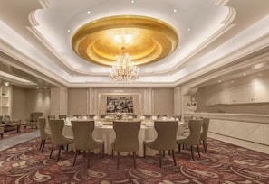 Uma sala de jantar formal com lustre, mesas redondas e carpete estampado.
