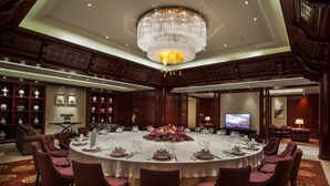 Une salle à manger élégante, avec une table ronde, des chaises à revêtement rouge, un lustre et un téléviseur en arrière-plan.