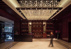 A lobby with a large chandelier, a reception desk, and shelves with bottles. - Holiday Inn Foshan Nanhai Central by IHG (Foshan)