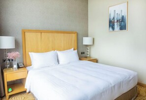 A hotel room with a large bed, two bedside tables, a lamp, a vase with flowers, and a painting on the wall. - Holiday Inn Foshan Nanhai Central by IHG (Foshan)
