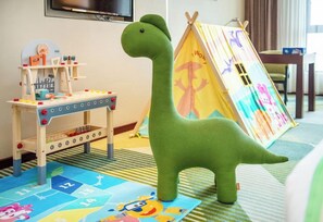 A green dinosaur toy, a wooden play table with a clock, and a colorful play mat. - Holiday Inn Foshan Nanhai Central by IHG (Foshan)
