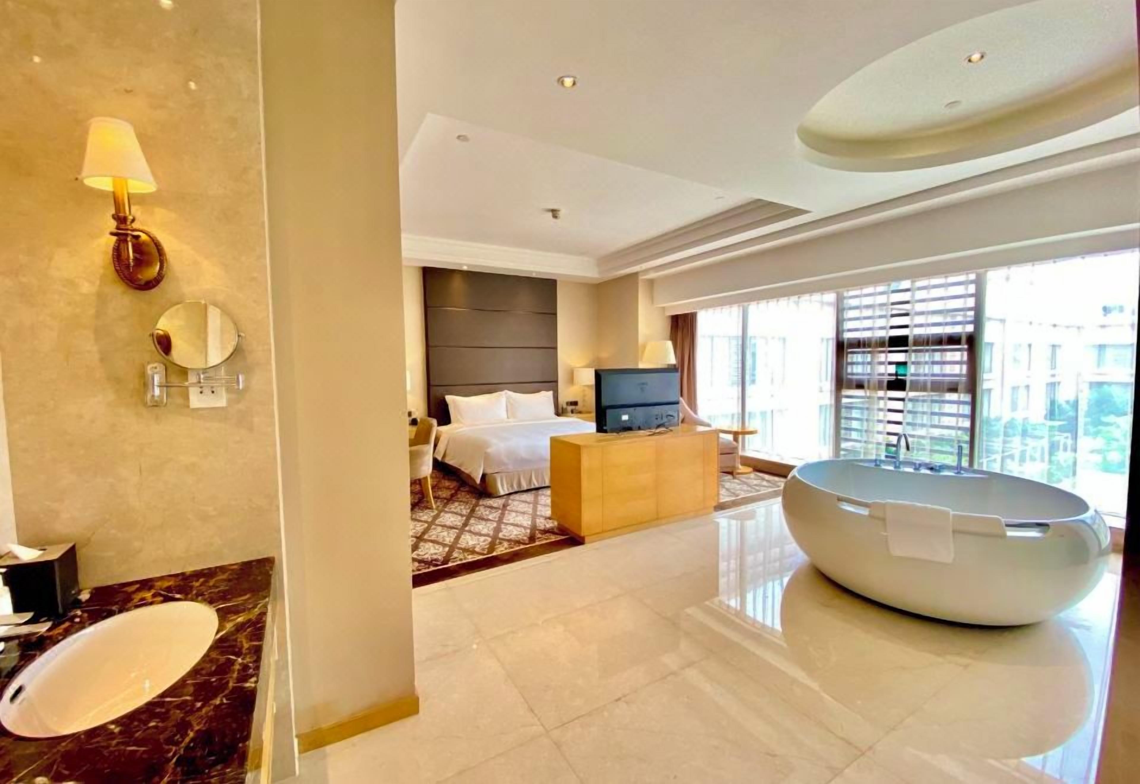 A modern hotel room with a large bathtub, a television, and a bed with a headboard.