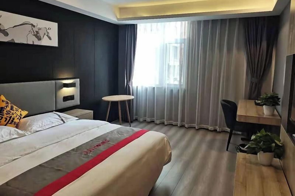 A hotel room with a bed, bedside table, desk, chair, and a window with curtains.