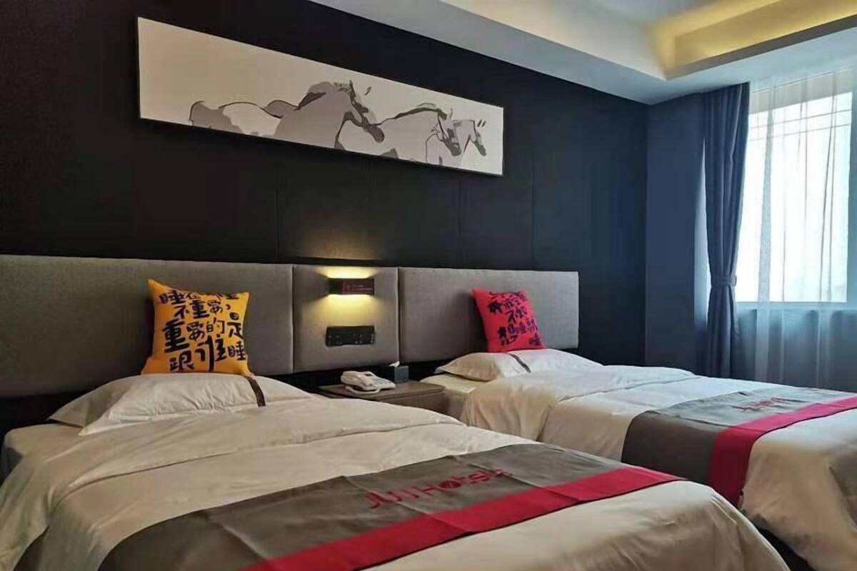 Habitació d'hotel amb dos llits, un quadre abstracte gran penjat sobre els llits i una finestra amb cortines.