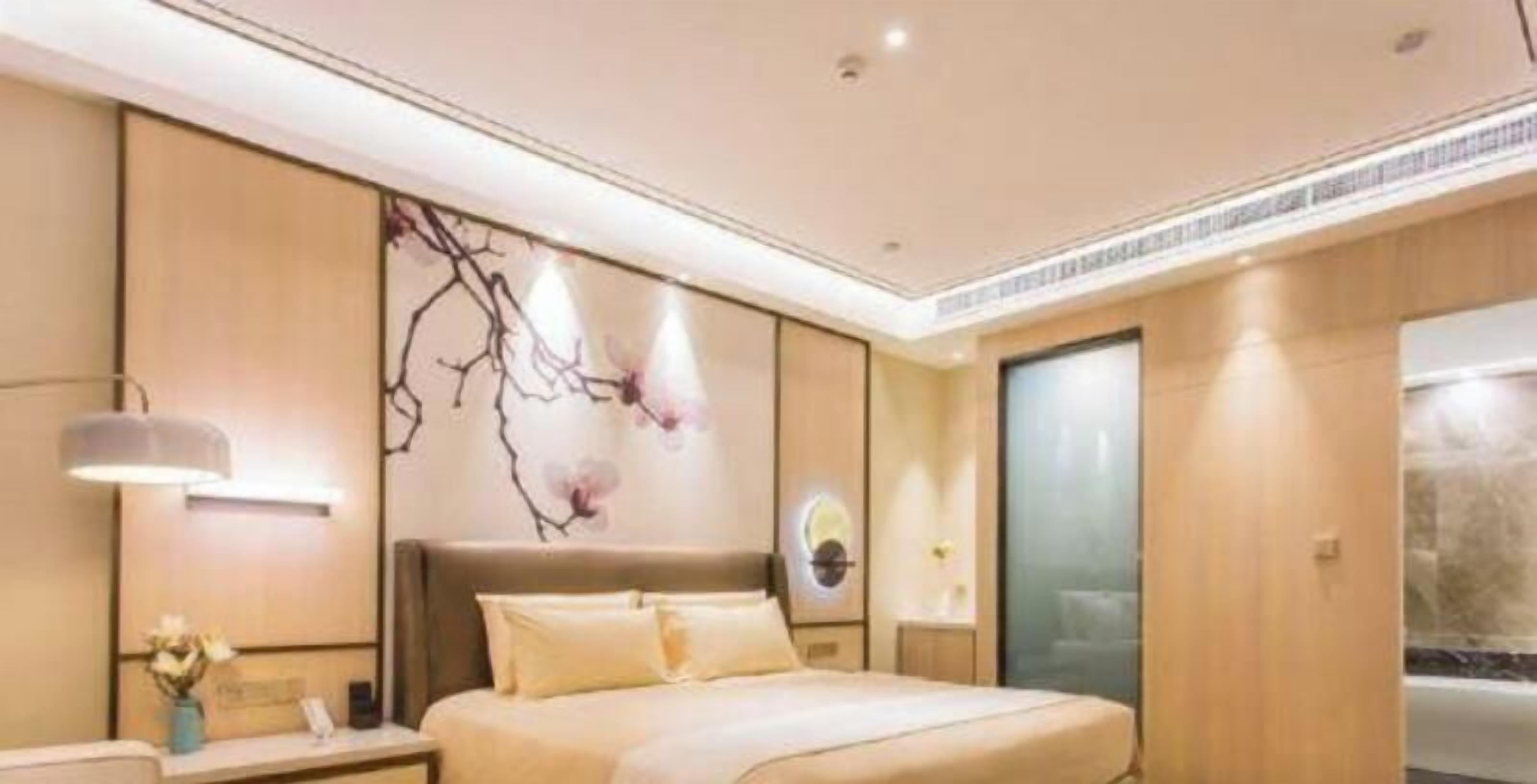A modern hotel room with a large bed, a nightstand, a wall-mounted lamp, and a decorative wall piece.