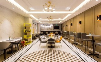 Un moderno vestíbulo de hotel con un área de comedor central, varias opciones de asientos y un llamativo patrón geométrico en el suelo.