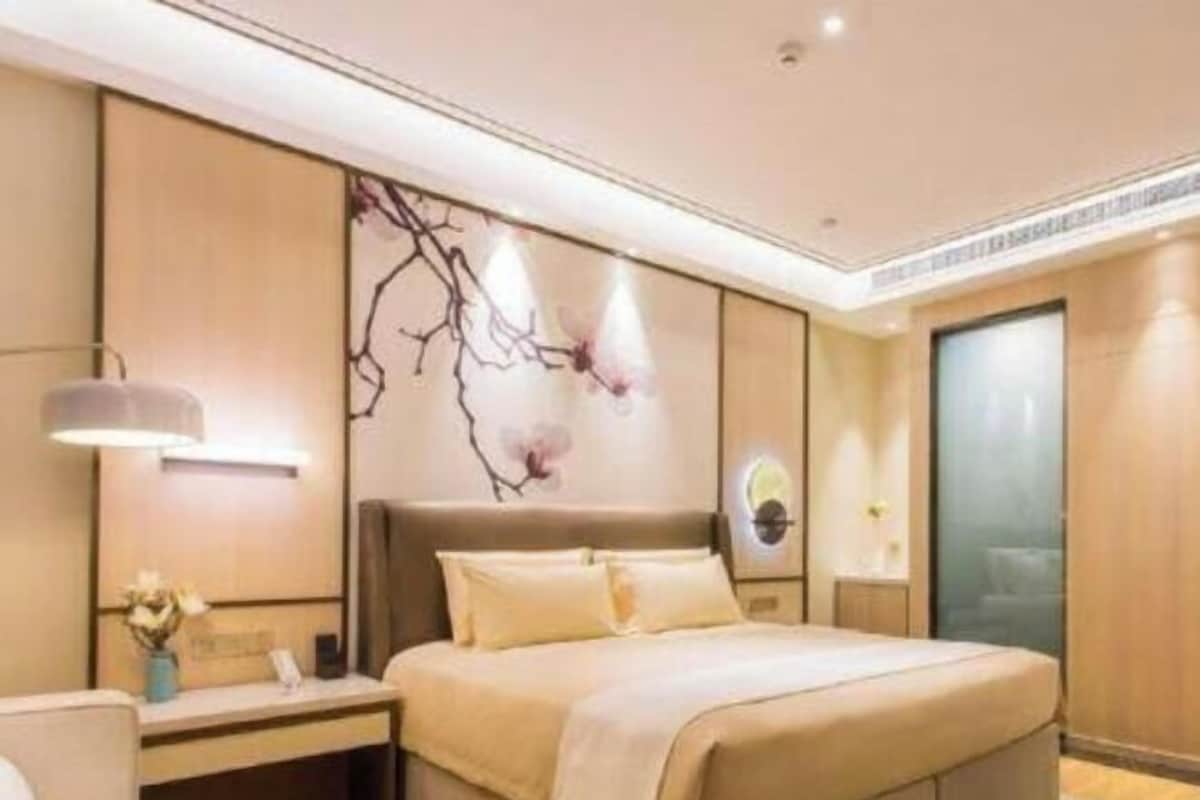 A modern hotel room with a large bed, a bedside table, a wall-mounted lamp, and a decorative wall piece.