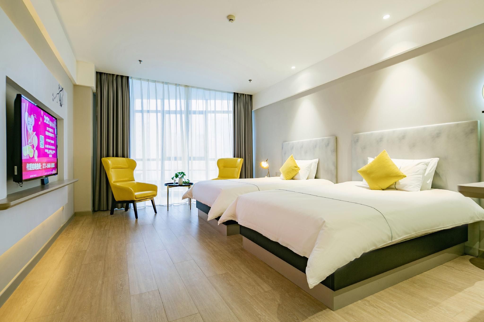 Een hotelkamer met een groot bed, twee stoelen, een televisie en een raam met gordijnen.