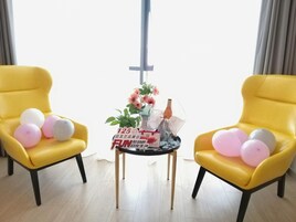 Una habitación con dos sillones amarillos, una mesita con globos, un florero con flores y una cruz colgada del techo.