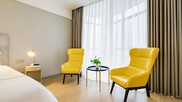 A hotel room with a bed, two yellow armchairs, a small round table with a plant, and a lamp on a nightstand. - Magnotel Yingda Road, Baoji (Baoji)
