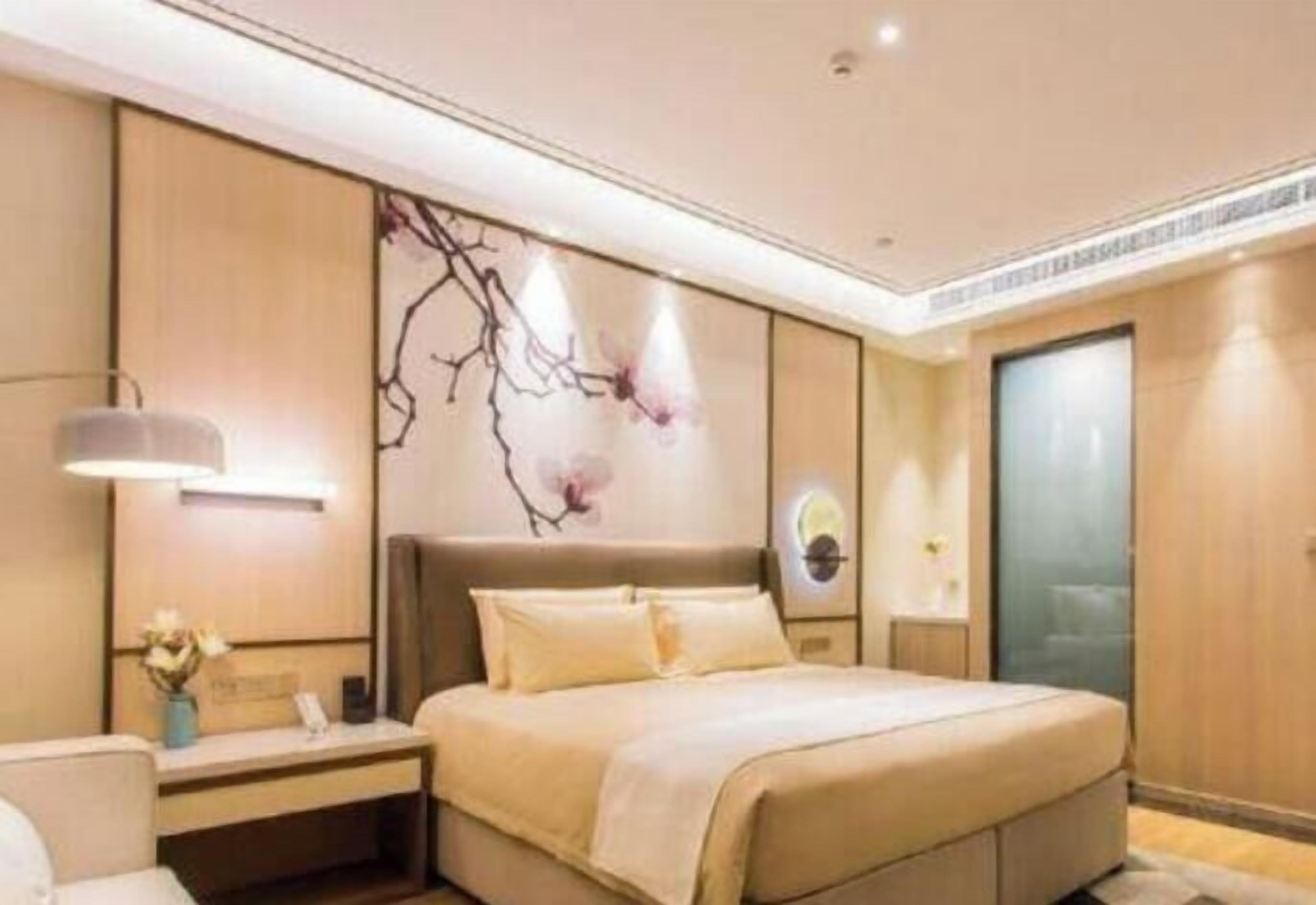A modern hotel room with a large bed, a nightstand, a wall-mounted lamp, and a decorative wall piece.