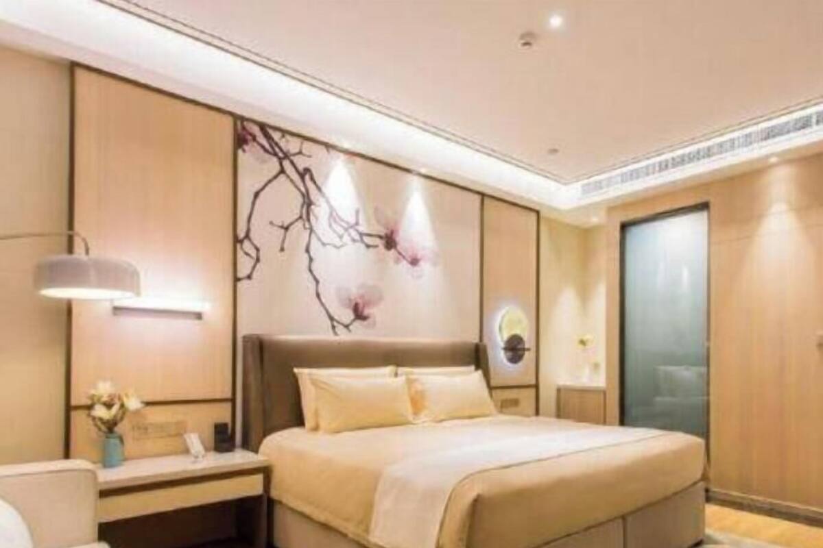 A modern hotel room with a large bed, a nightstand, a wall-mounted lamp, and a decorative wall piece.