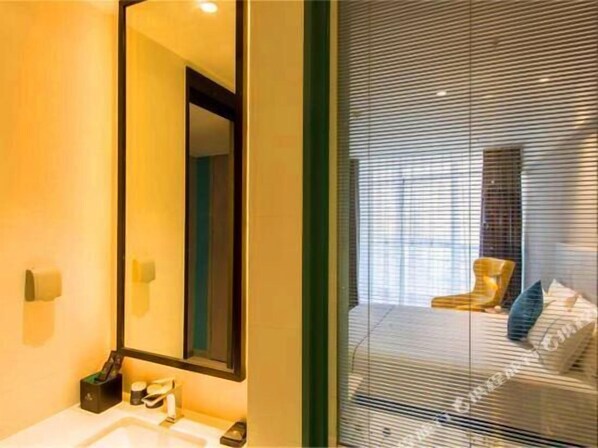A hotel room with a large mirror, a sink, and a window with blinds. - Magnotel (Baoji)