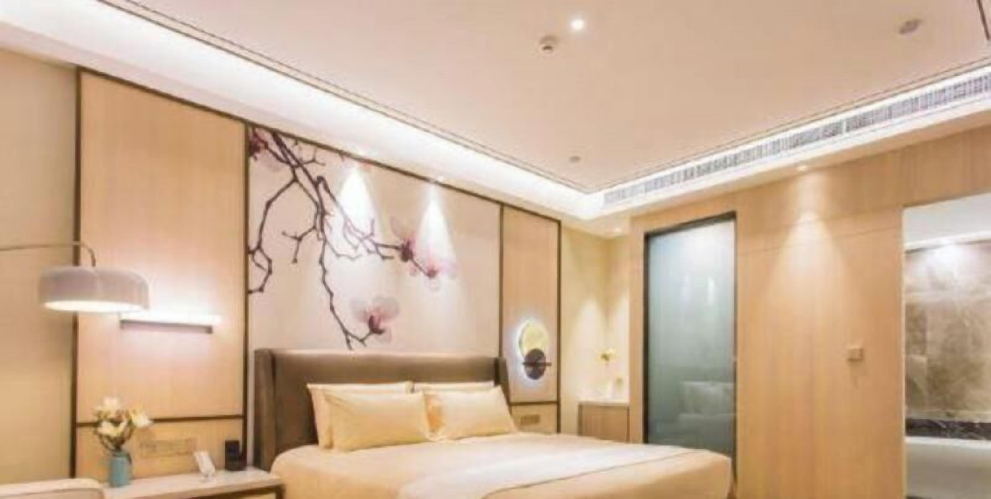 A modern hotel room with a large bed, a nightstand, a wall-mounted lamp, and a decorative wall piece.