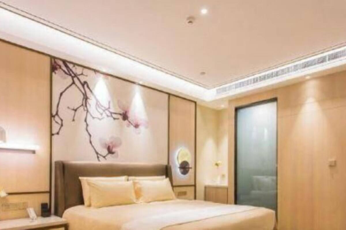 A modern hotel room with a large bed, a bedside table, a wall-mounted lamp, and a decorative wall piece.