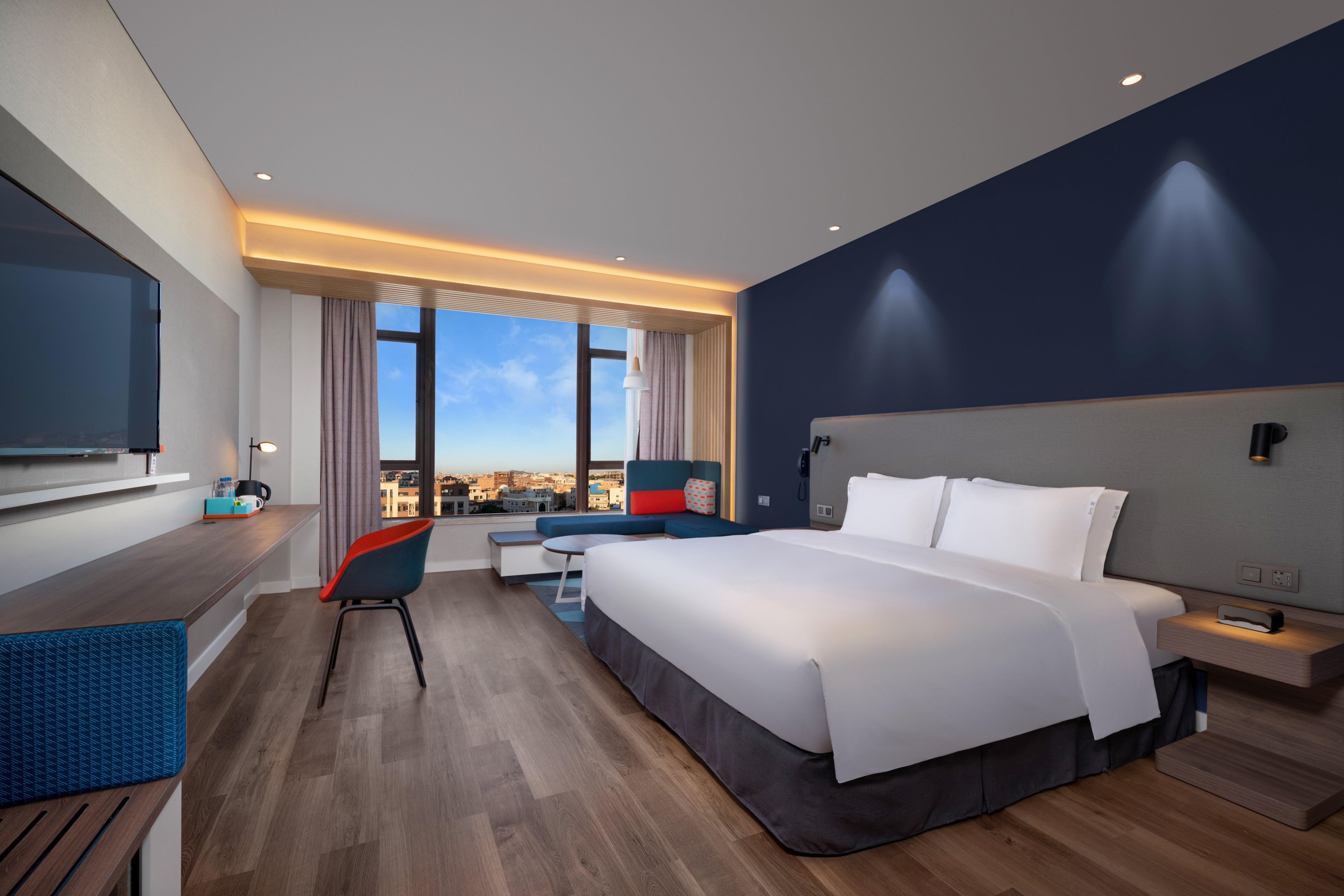 Una camera d'albergo moderna con un letto grande, una scrivania, una sedia e vista sulla città.
