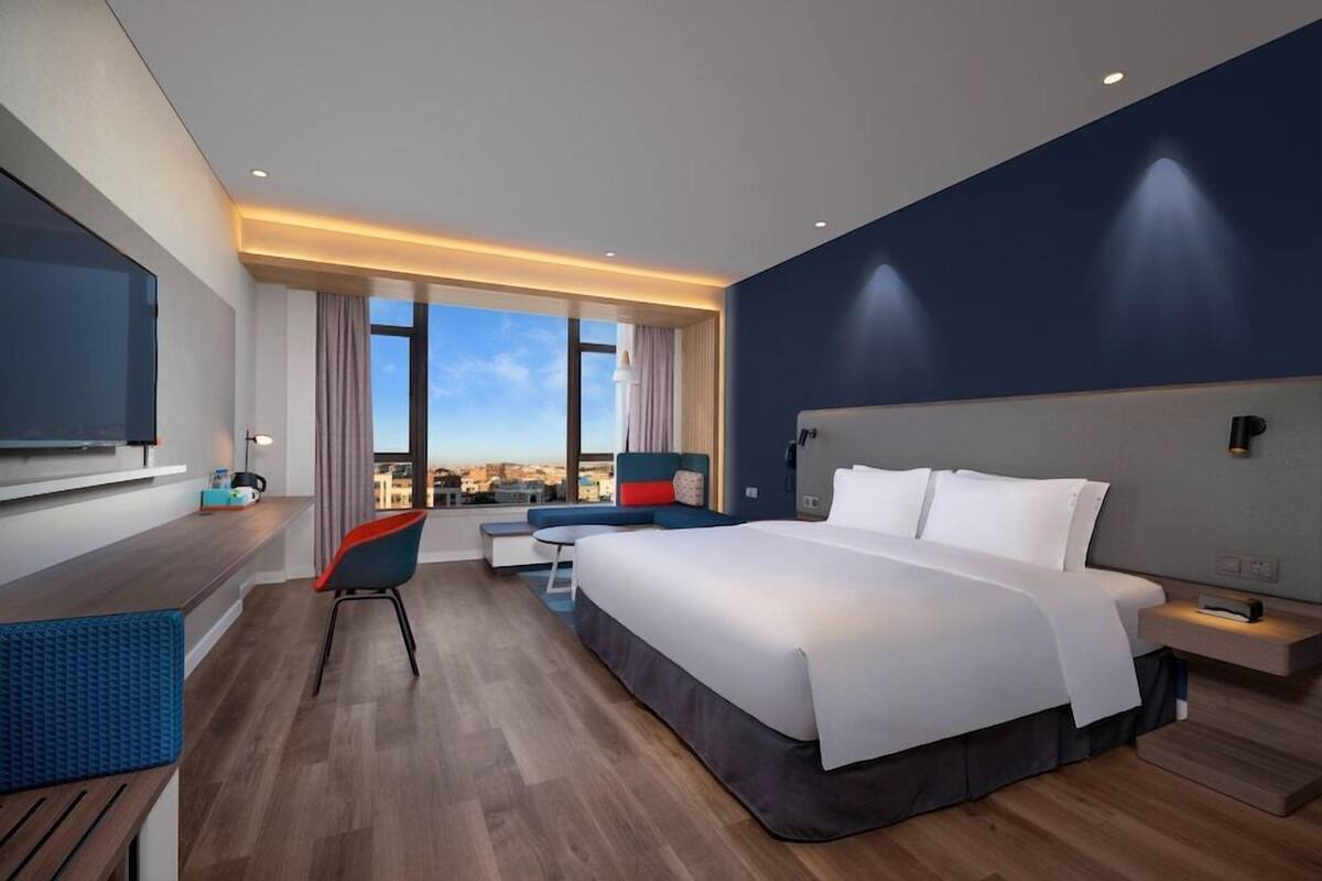 Habitación de hotel moderna con una cama grande, zona de estar con vistas, televisor de pantalla plana y vista panorámica de la ciudad.