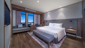 A modern hotel room with a large bed, a sofa, a bench, and a view of the city. - Holiday Inn Express Jinjiang Anhai (Quanzhou)