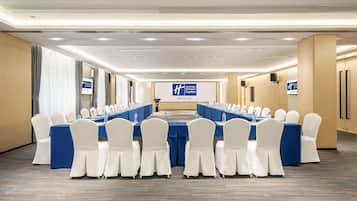 Un salón de conferencias con una larga mesa, sillas blancas y manteles azules.