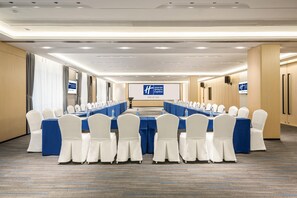 Un salón de conferencias con una larga mesa, sillas blancas y manteles azules.