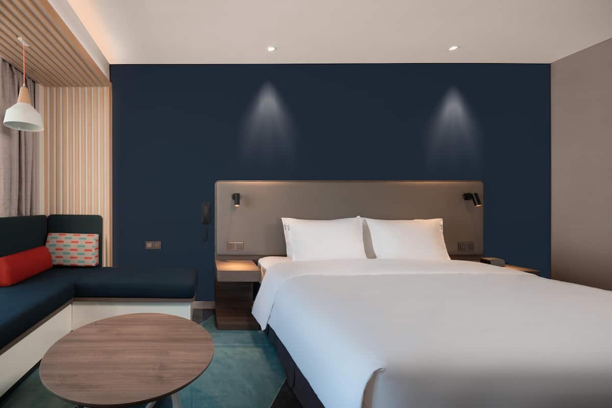 Una habitación de hotel moderna con una cama grande, un sofá, una mesita y una lámpara de pared.