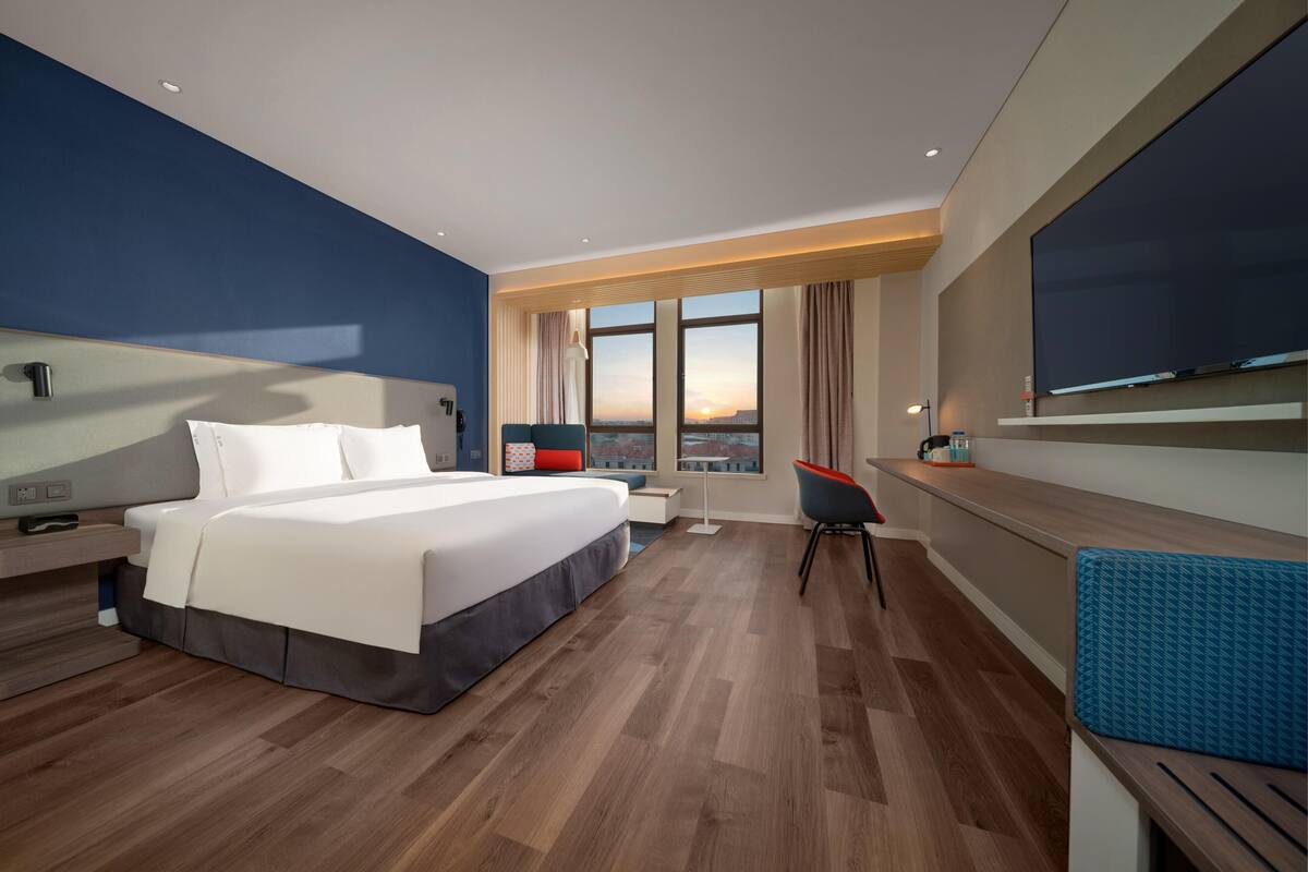 Una habitación de hotel moderna con una cama grande, un escritorio, una silla y un televisor montado en la pared.