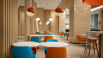 A modern dining area with round tables and colorful chairs, featuring a wooden panel wall and hanging pendant lights.
